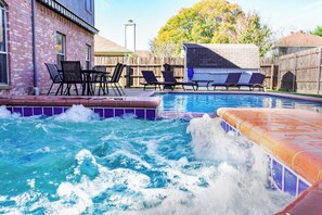 Una piscina amb gandules i un banyera d'hidromassatge, envoltada per una tanca de fusta i un edifici de maó.