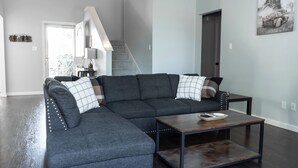A modern living room with a sectional sofa, a coffee table, and a staircase leading to another level. - Sleeps 12 - Pool, Hot Tub & Game Room (Grand Prairie)
