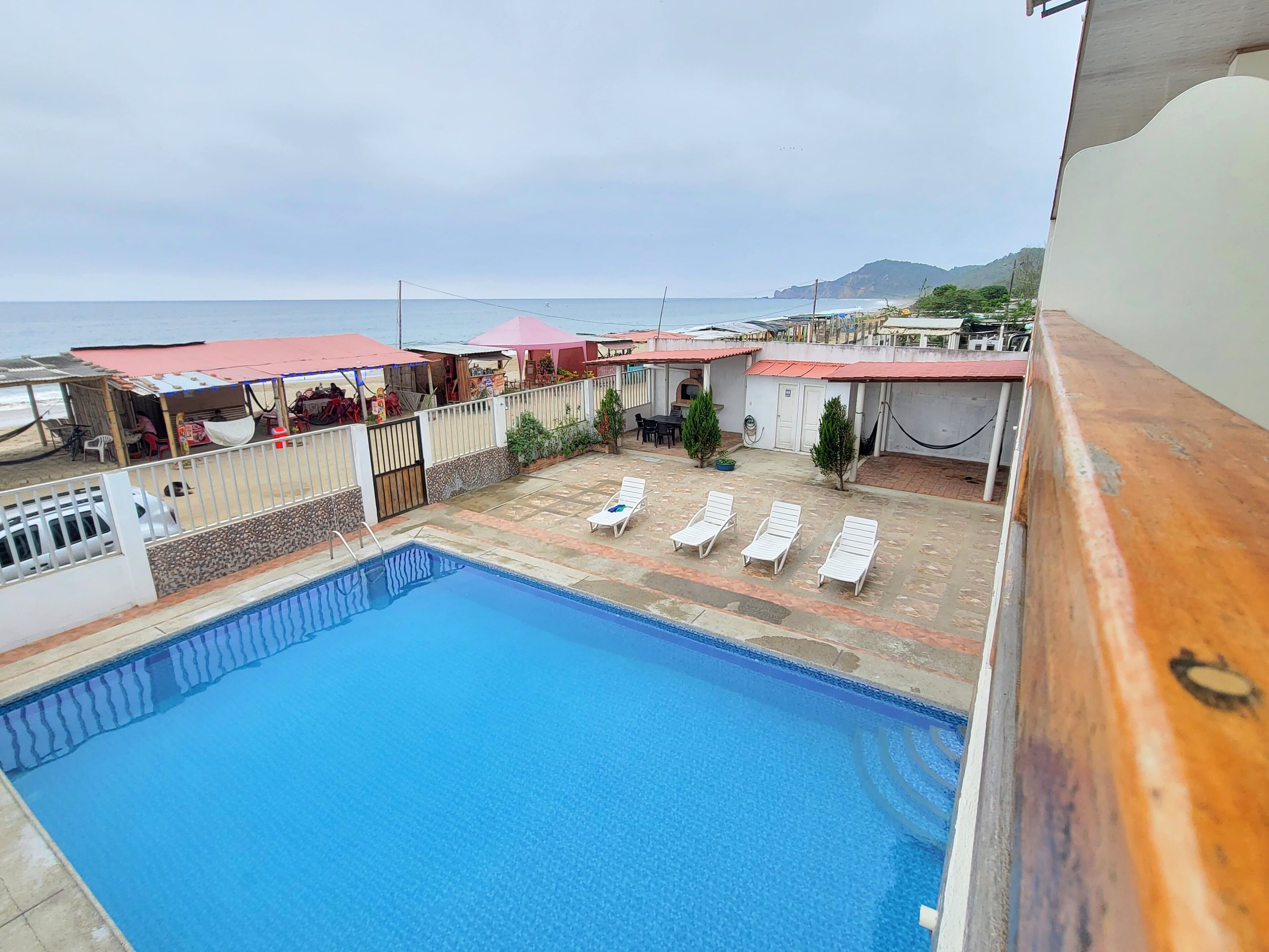 Una piscina con sillas de descanso blancas, un área de estar cubierta y vista al mar.