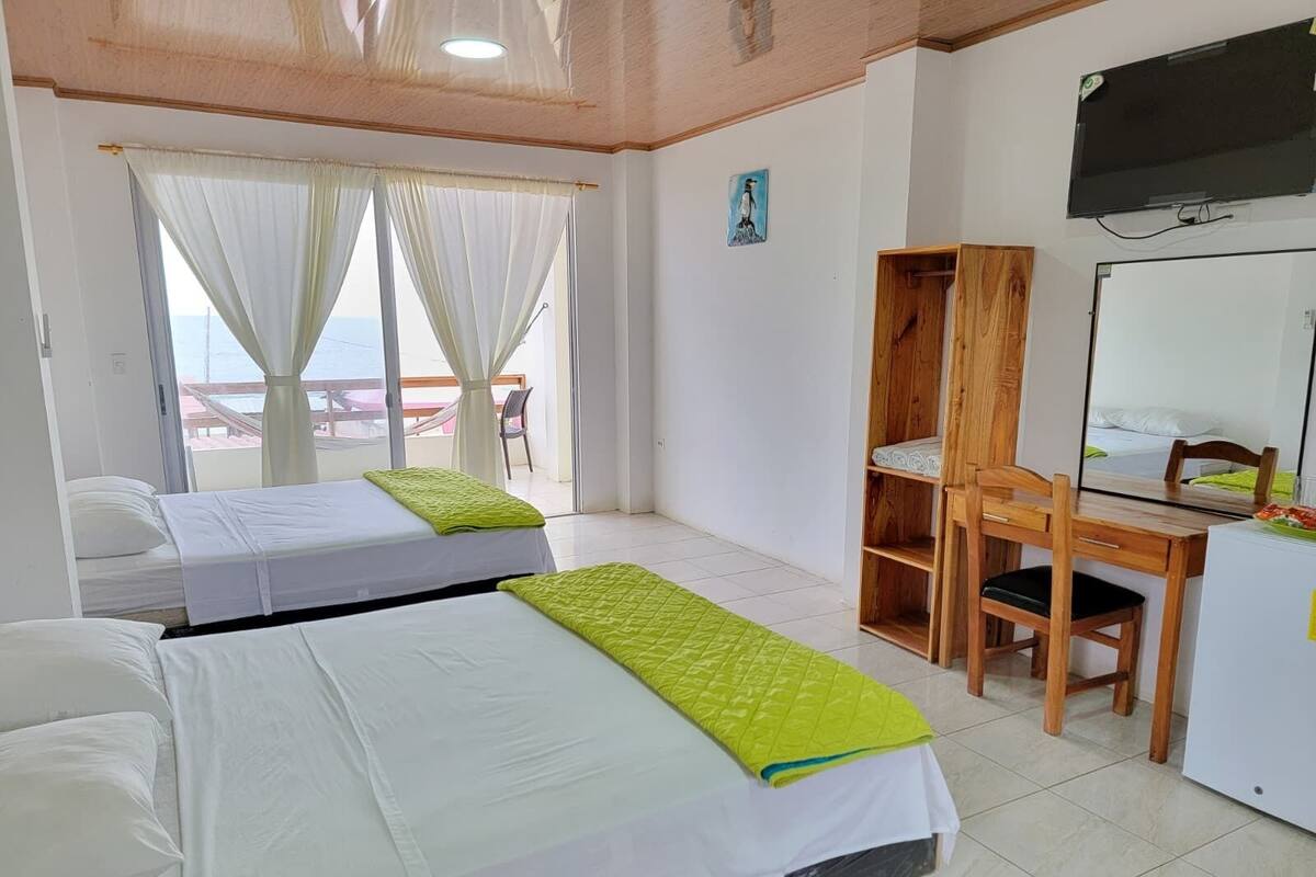 Ein Hotelzimmer mit zwei Betten, einem Schreibtisch, einem Sessel, einem Fernseher und einem Balkon mit Aussicht.