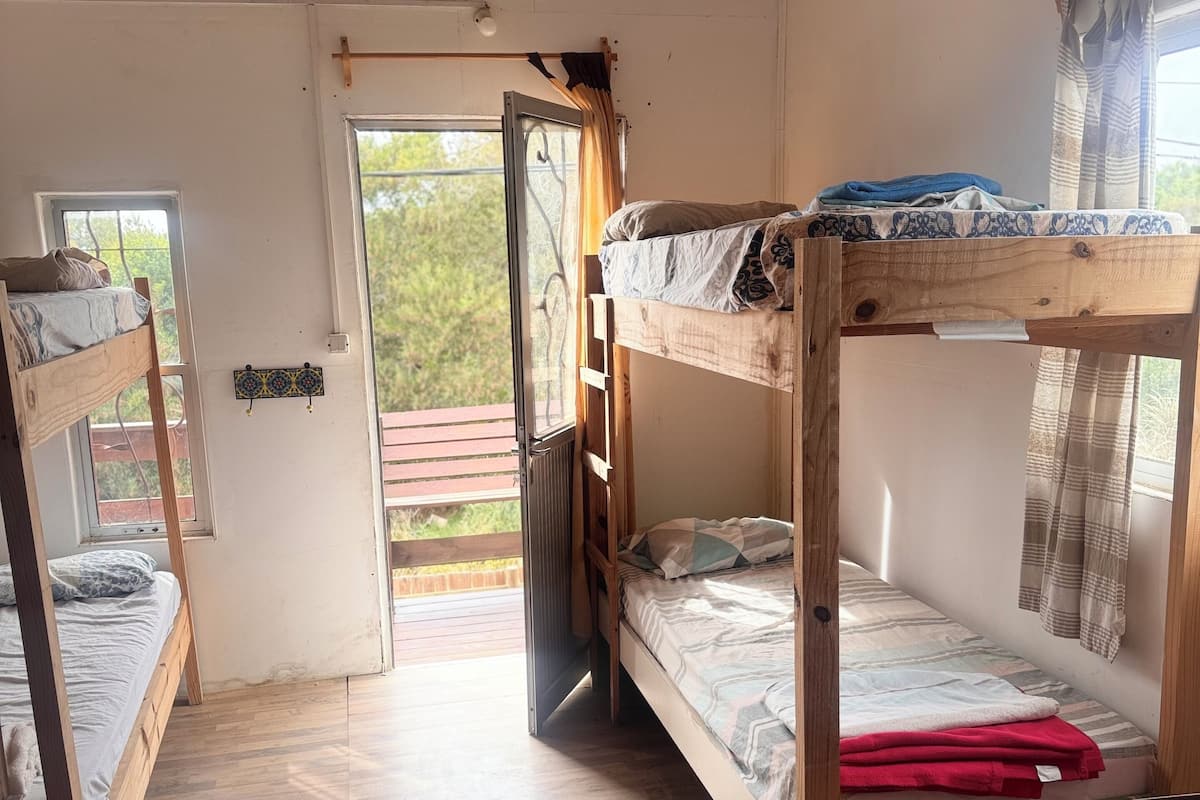 Una stanza con due letti a castello, pavimento in legno, una finestra con tende e una porta che dà sull'esterno.