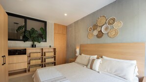 Una camera da letto moderna con un letto grande, una testiera in legno e uno specchio fissato alla parete. Sono presenti contenitori portaoggetti con cesti e una pianta in vaso.
