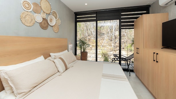Una camera da letto moderna con un letto grande, una TV e un balcone con vista sugli alberi.