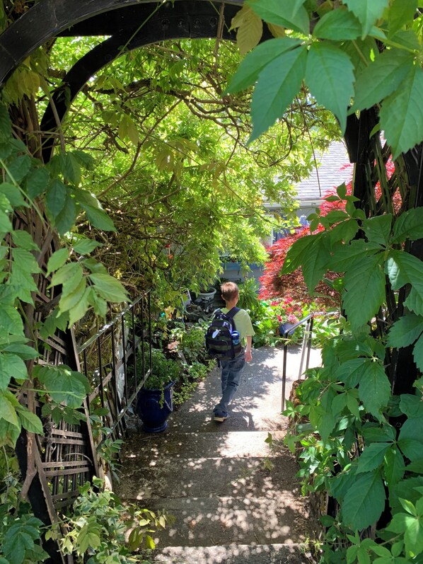 Un sentier étroit bordé d’une végétation luxuriante et surmonté d’une arche en bois.