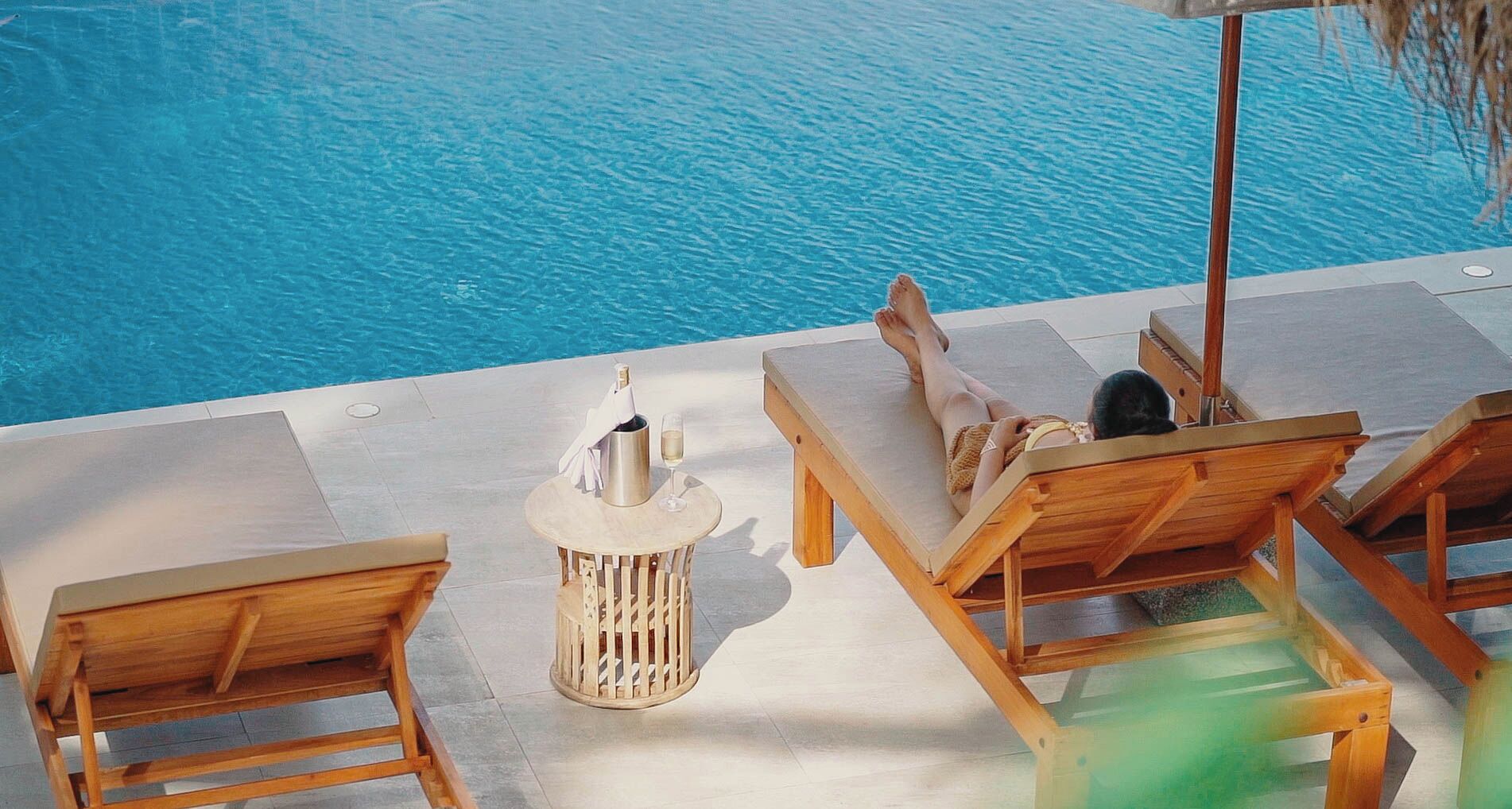 A poolside area with lounge chairs and a table with a bottle and glass.