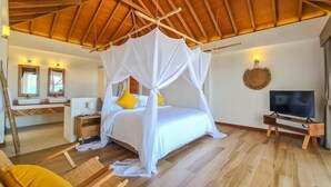 A bedroom with a canopy bed, wooden flooring, a television, and a bathroom with a vanity and mirrors. - the nest private beach resort (Chumphon)