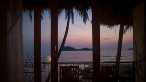 A wooden deck with two wooden chairs, overlooking a beach with palm trees and a sunset. - the nest private beach resort (Chumphon)