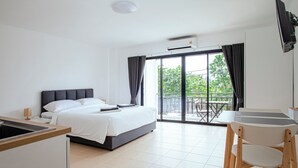 Ein modernes Hotelzimmer mit einem Bett, einem Essbereich mit Stühlen, einer Küchenzeile und einem Balkon mit Blick auf Bäume.