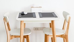 Ein moderner Essbereich mit einem weißen Tisch, zwei Holzstühlen und einem an der Wand befestigten Flachbildfernseher.