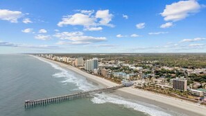 A coastal cityscape with a long pier extending into the ocean, high-rise buildings, and a beach. - Sand Dollar | Spacious 4BR w/ Ocean Views + Pool (Myrtle Beach)
