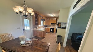 A dining area with a wooden table, chairs, a chandelier, and a view into the kitchen. - Elk River Retreat, in Rogersville AL (Rogersville)