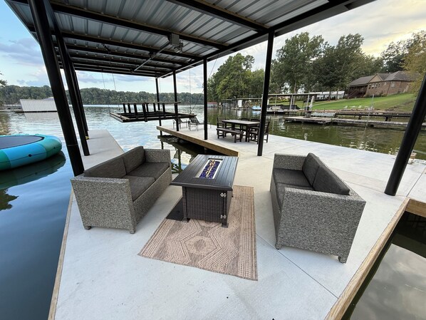 An outdoor patio with wicker furniture, a fire pit, and a view of a lake and dock.