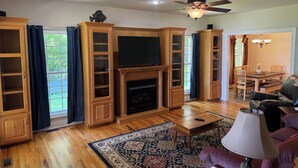 A living room with wooden cabinets, a fireplace, a television, and a dining area with chairs. - Elk River Retreat, in Rogersville AL (Rogersville)