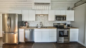 A modern kitchen with stainless steel appliances, white cabinetry, and a wooden countertop. - Cozy, lakeside tiny home in Arkansas farm country (Parkin)