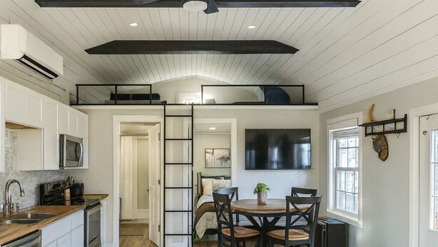 A spacious kitchen with modern appliances, a dining area with a round table and chairs, and a cozy seating area with a leather chair. - Cozy, lakeside tiny home in Arkansas farm country (Parkin)
