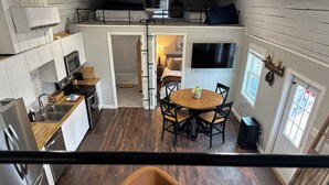 A compact kitchen with modern appliances, a dining area with a round table and chairs, and a cozy seating area with a brown chair. - Cozy, lakeside tiny home in Arkansas farm country (Parkin)