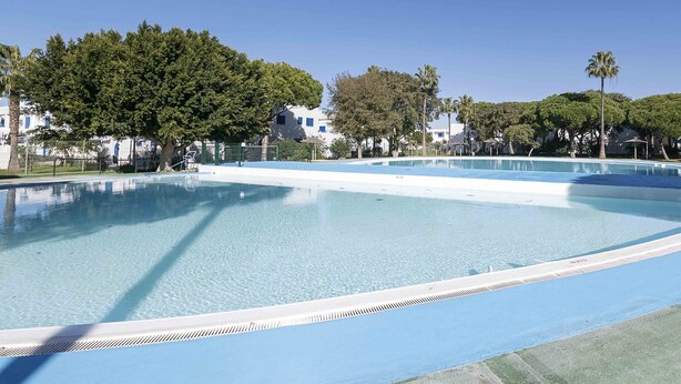 Una amplia piscina al aire libre con agua cristalina y azul, rodeada de árboles y edificios.