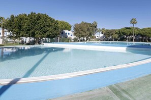 Une grande piscine extérieure à l’eau d’un bleu limpide, entourée d’arbres et de bâtiments.