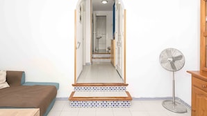 Un pasillo estrecho con una cama a la izquierda, un ventilador a la derecha y una puerta al final que da a un baño.