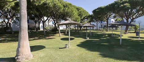 A park with trees, grass, and thatched-roof gazebos.