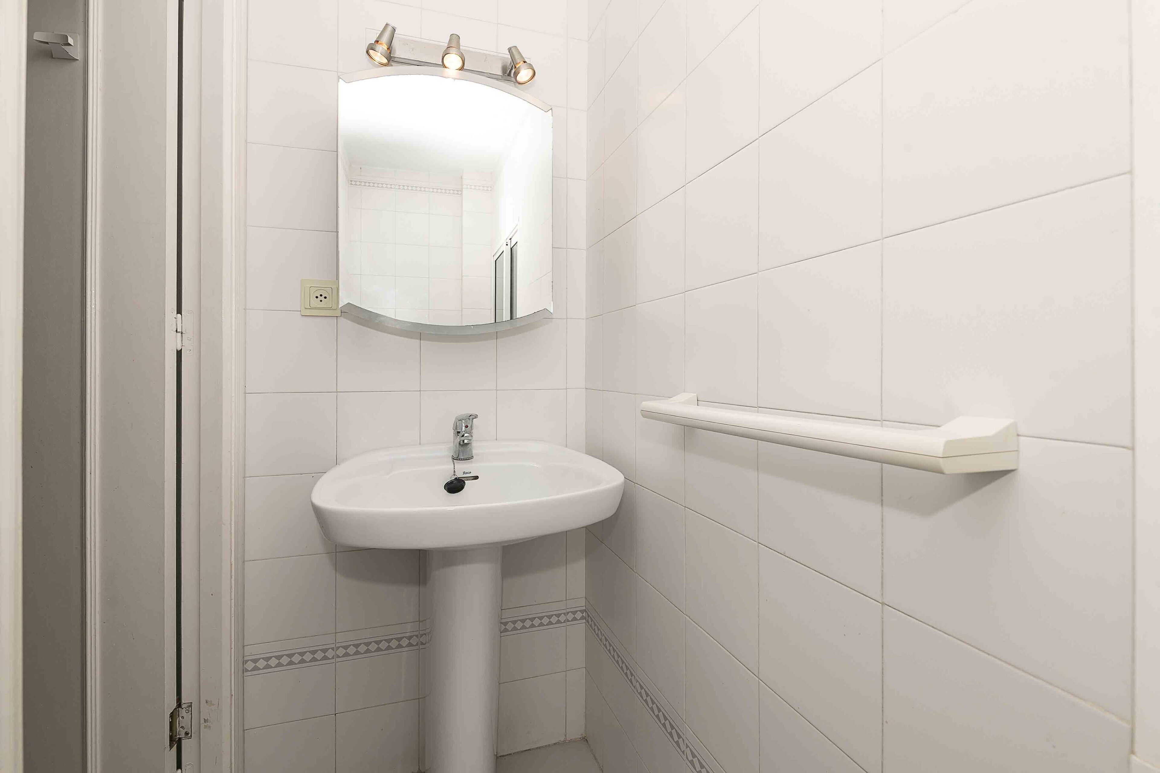 Un baño con lavamanos blanco, un espejo y un perchero para toallas.