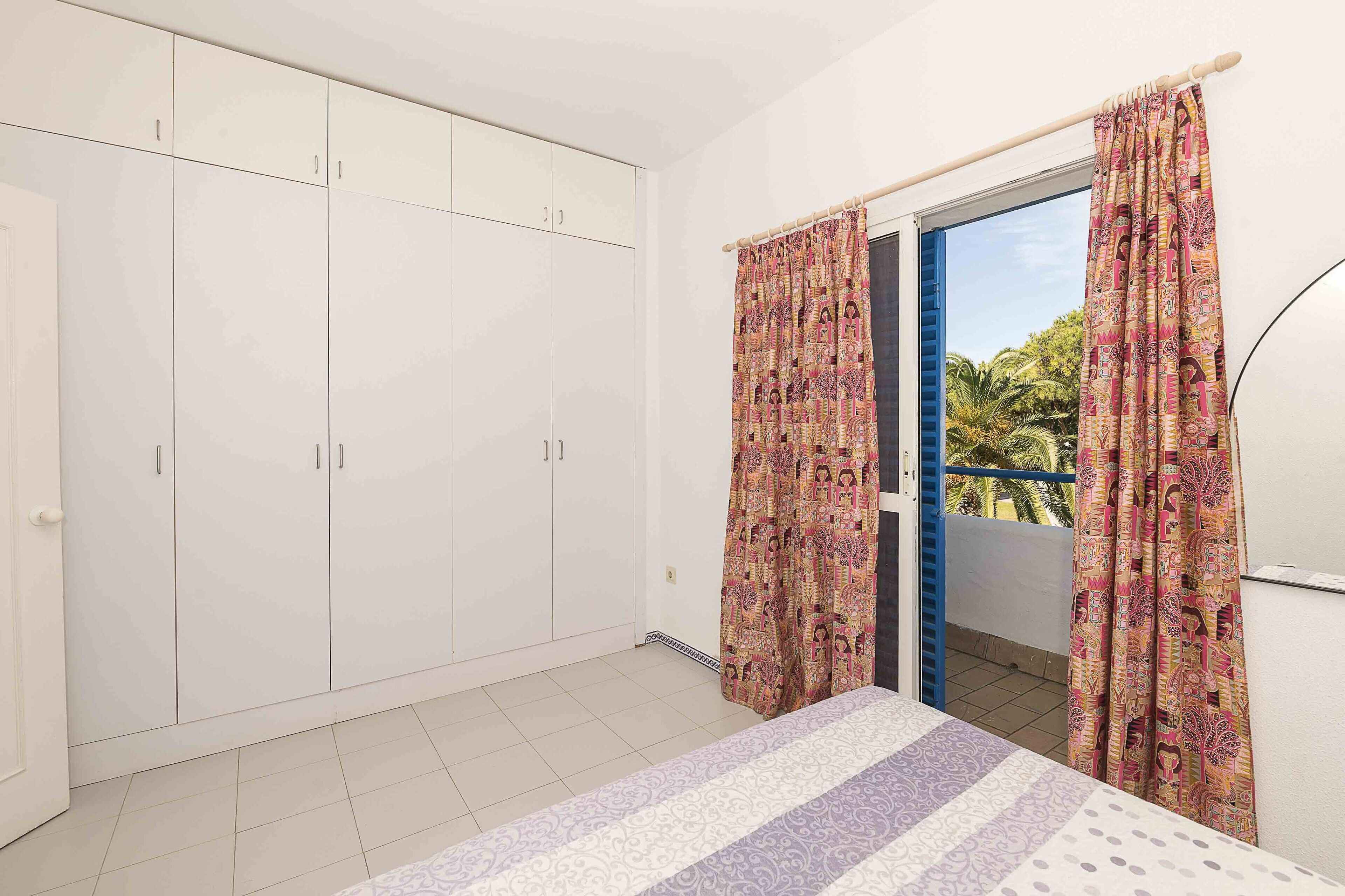 Un dormitorio con un armario grande, una cama con ropa de cama estampada y un balcón con cortinas decorativas.