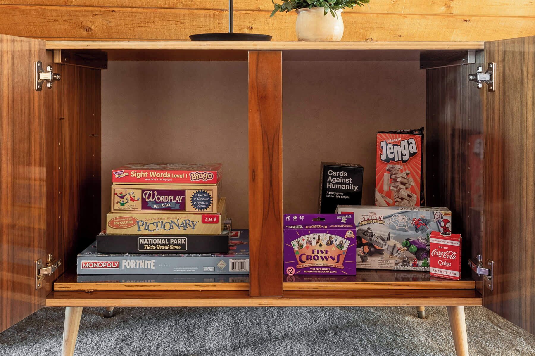 Un mueble de madera con diversos juegos de mesa y una caja de Coca-Cola.