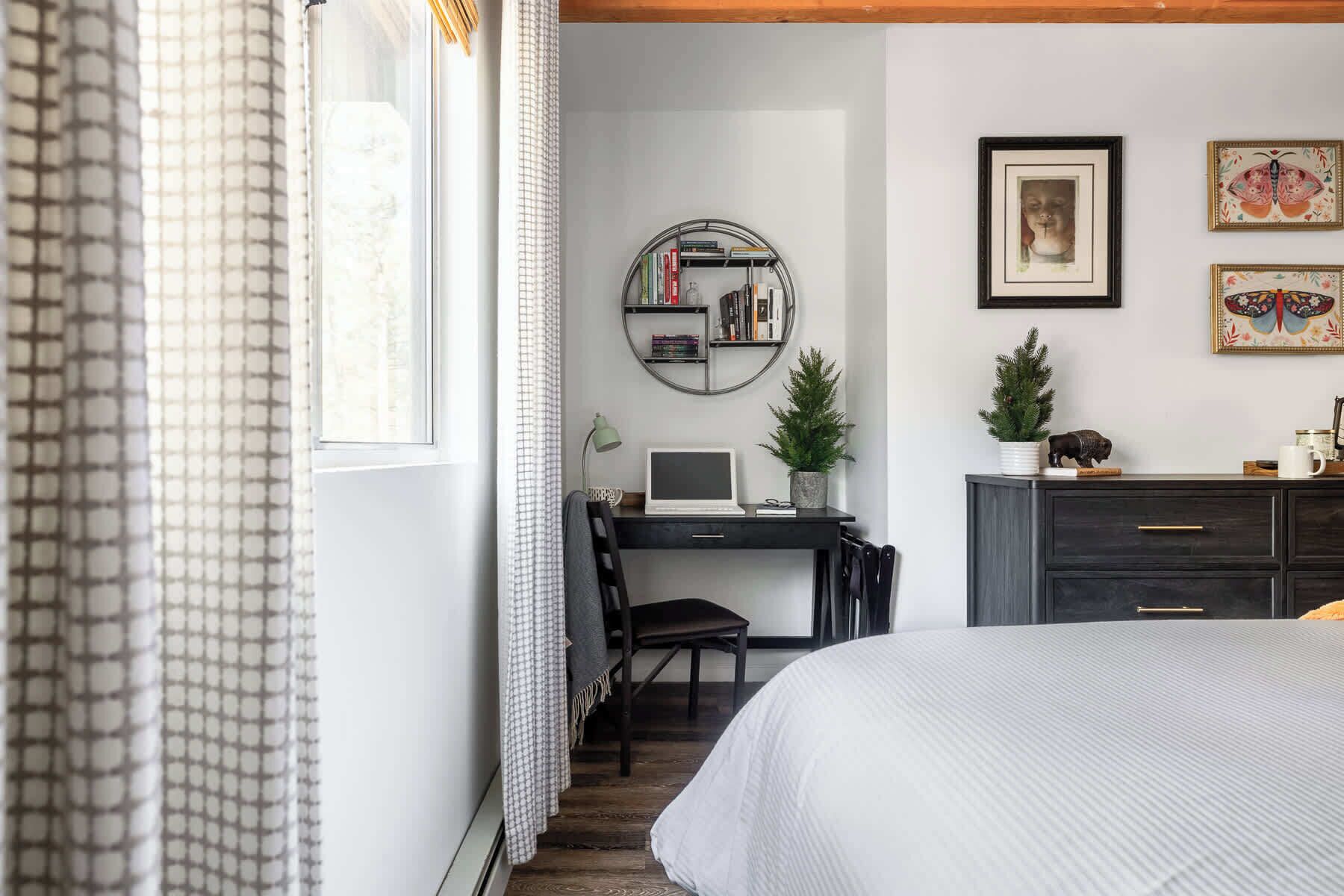 A bedroom with a bed, a desk with a laptop, a bookshelf, and a dresser.