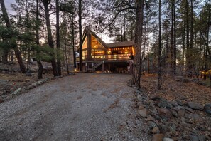 A lodge with a prominent wooden structure, a gravel driveway, and surrounding pine trees. - Cozy Chalet in the Pines (Munds Park)