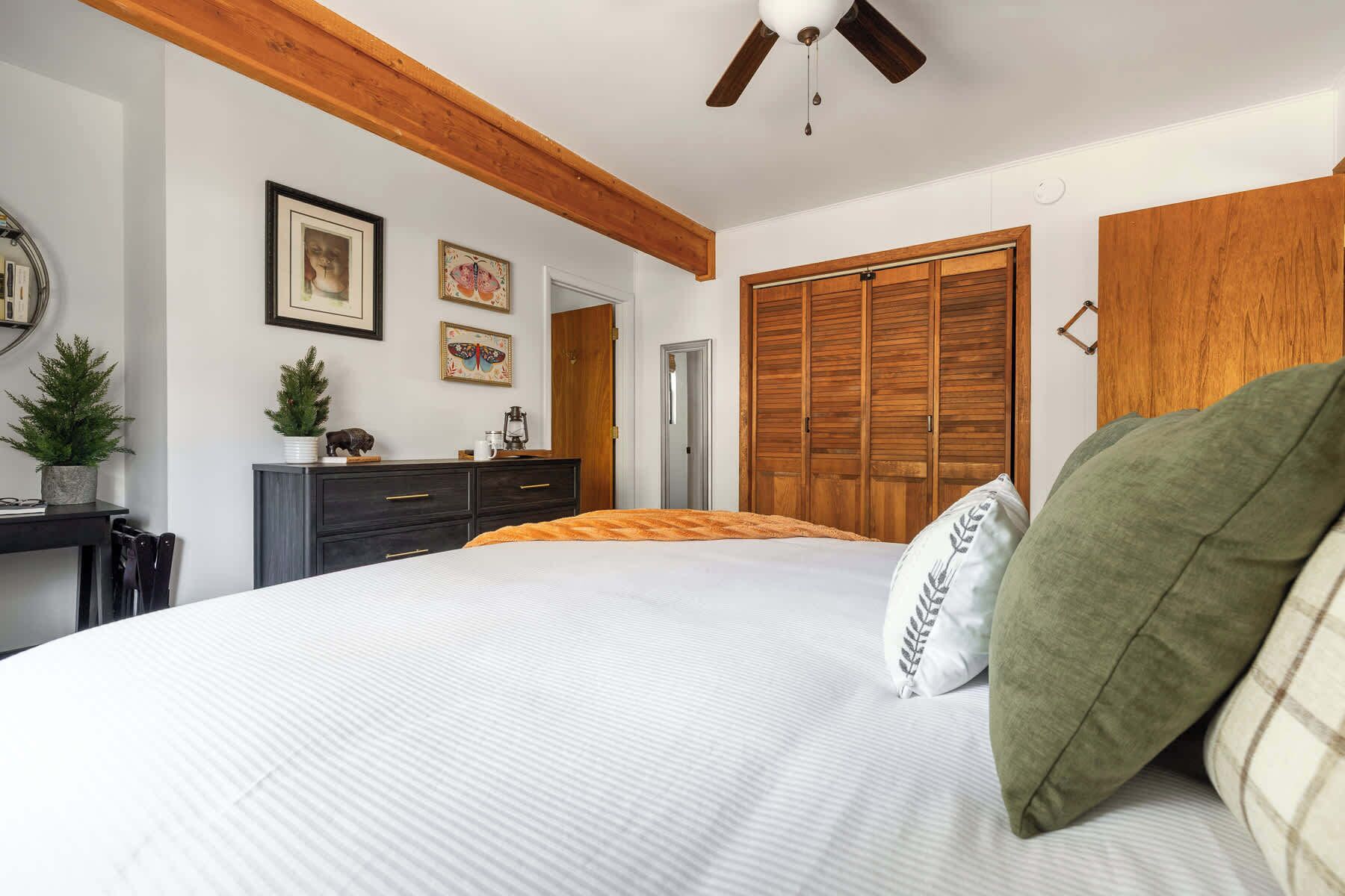 A bedroom with a bed, wooden wardrobe, and a ceiling fan.