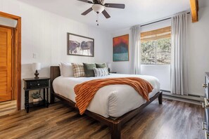 A bedroom with a wooden bed, a nightstand, a ceiling fan, and a window with curtains. - Cozy Chalet in the Pines (Munds Park)