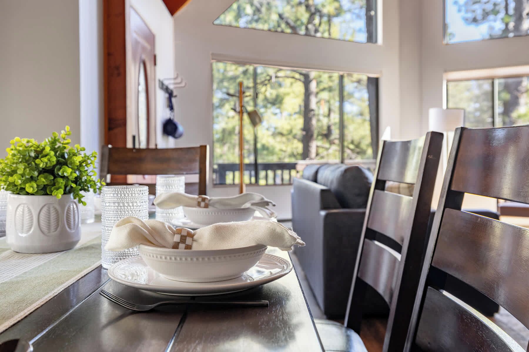 A dining area with a wooden table, white plates, and a potted plant.