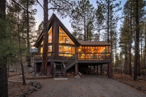 Une cabane dotée d’une grande terrasse, d’un escalier menant à l’étage supérieur et offrant une vue sur la forêt environnante.