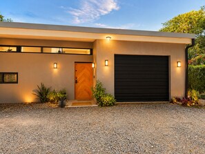 A modern house with a wooden door, a garage door, and a gravel driveway. - 3-bedroom house with private pool, AC, fitness center-5min from the sand. (Provincia de Guanacaste)
