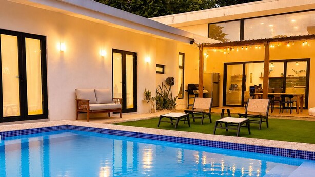 Ein Schwimmbad mit gefliestem Rand, umgeben von einer Terrasse mit Stühlen und einer Sitzecke.