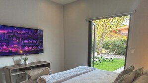 Ein Schlafzimmer mit einem großen Bett, einem an der Wand montierten Fernseher und einer Glastür, die zu einem Garten führt.