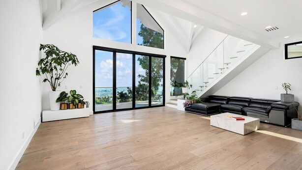 A spacious living area with a large black leather sofa, a white coffee table, and a view of the city through floor-to-ceiling windows. - Modern Luxury in Peaceful Hollywood Hills with Epic City Views (Los Angeles)