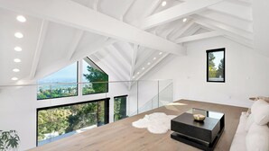 A spacious room with a high ceiling, large windows offering a city view, a modern black coffee table, and a white sofa. - Modern Luxury in Peaceful Hollywood Hills with Epic City Views (Los Angeles)