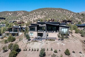 Una casa moderna de dos pisos con techo plano, ventanas amplias y un patio.