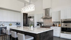 A modern kitchen with white cabinetry, a large island with bar stools, stainless steel appliances, and a decorative chandelier. - Juniper Ridge at Cordillera Valley Club (Edwards)