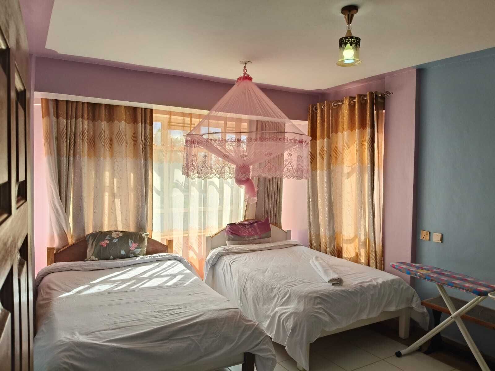 A room with two beds, a mosquito net, curtains, and a small ironing board.