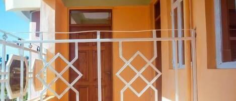 A narrow corridor with a white metal gate, a wooden door, and a ceiling fan.