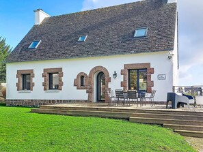Ein weißes Gebäude mit Steinverzierungen, einem Ziegeldach und einer Terrasse mit Außenbestuhlung.