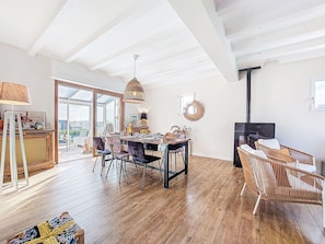 A spacious living area with a wooden floor, a dining table with chairs, a wicker sofa, and a fireplace. - Le Clozic by Interhome (Locquirec)