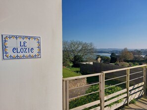 Un balcone con vista su un paesaggio costiero, un cartello con la scritta 'LE CLOZIC' e un muro in pietra.