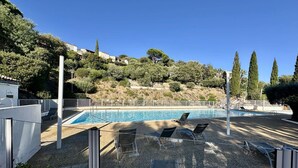 En swimmingpool med solstolar, omgiven av ett område med grus och träd.