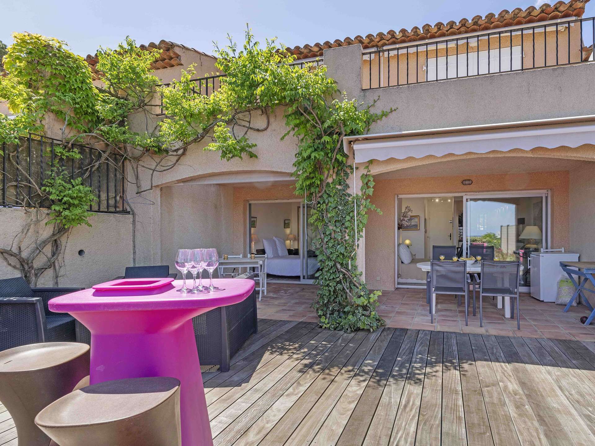 An outdoor patio with a pink table, chairs, and a small garden area.