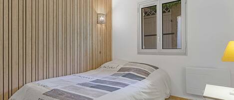 Un dormitorio con cama, ventana, luz empotrada en la pared y radiador.