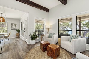 Ein geräumiges Wohnzimmer mit großem Fenster, einem weißen Sofa, einem Couchtisch und einem Essbereich mit Tisch und Stühlen.