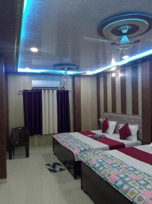 A hotel room with a bed, a desk, a chair, and a ceiling fan. - Hotel Yash Dham (Ayodhya)